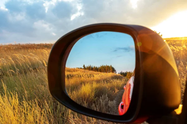 Reflected field and forest in the rearview mirror at sunset. The concept of car eco travel around your country, travel to a future or a past, ways to change