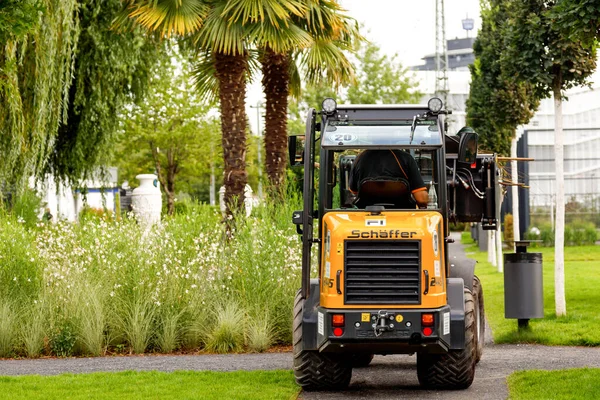 Heilbronn, Almanya - 12 Ağustos 2019. Federal Garden Show 2019 BUGA Heilbronn boyunca modern evlerin yakınındaki bölgeyi küçük bir traktör temizliyor..