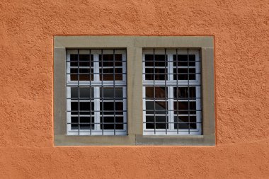 Turuncu taştan bir duvara dayanan metal parmaklıklı eski bir pencere..