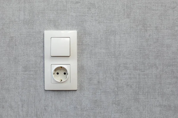 Електричний вимикач світла і заземлена розетка на порожній сірій стіні . — стокове фото