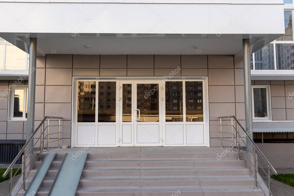 Entrance lobby with a metal canopy, ramp and plastic doors in apartment building. Social housing