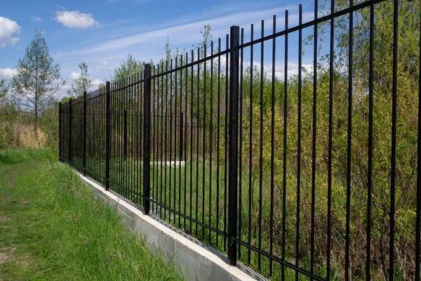 Mavi gökyüzüne karşı beton temeli olan uzun, şeffaf metal bir çit. Çapraz düzenleme.