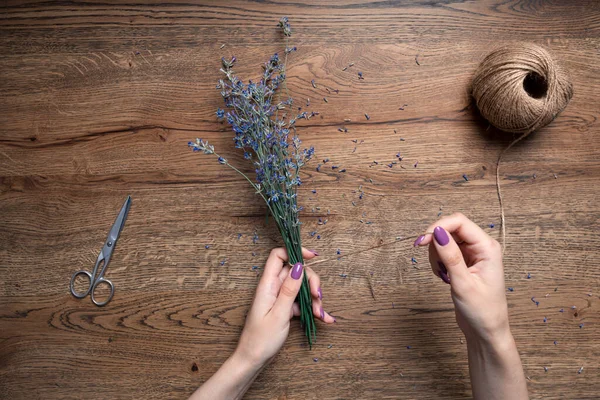 Beautiful female hands tie bunch of dry lavender on the background of oak table. top view — Stock Photo, Image