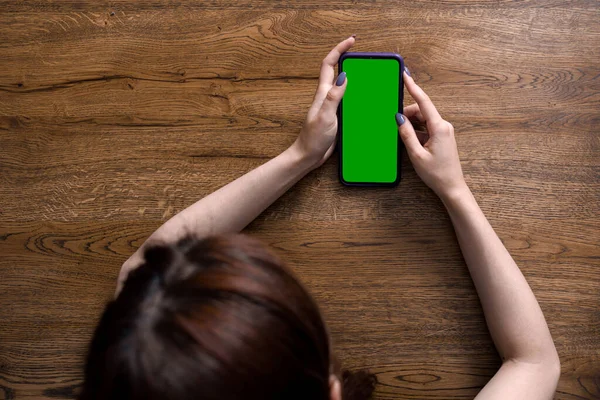 Closeup image of young woman holding smartphone on wooden background. Empty green screen for inserting your own picture or text — Stock Photo, Image