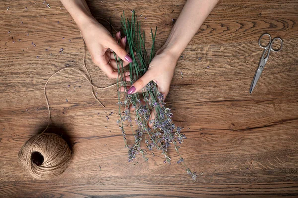 Beautiful female hands tie bunch of dry lavender on the background of oak table. top view — Stock Photo, Image