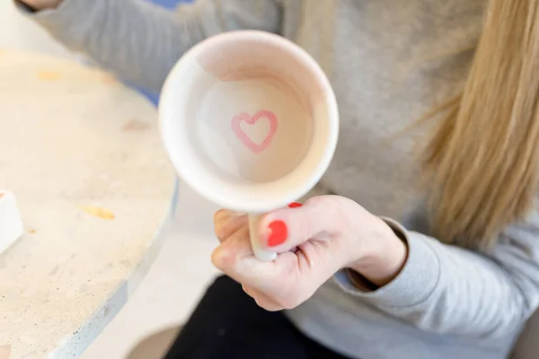 Ppainted pink heart onbottom of cup. Woman shows results of her work. Selective focus. — Stock Photo, Image