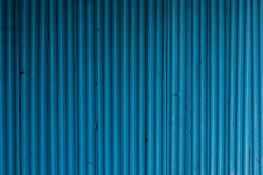 Çatlak, küçük kusurlar ve gölgeler olan binanın mavi ahşap ön cephesi. Çitlerdeki yıpranmış boyalar ya da parlak güneş ışığında duvarlar..