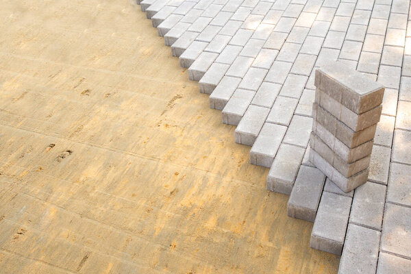 Вид сверху на край поверхности с уложенными плитами тротуаров. Видима поверхность с песчаной смесью. Пачка тротуарных плит готова к укладке