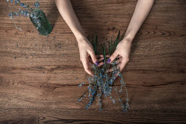 Hermosas manos femeninas sostienen ramitas de lavanda seca en el fondo de la mesa de roble — Foto de Stock