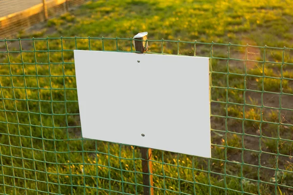 Empty sign on fence made of green plastic grating. Soft roll of vinyl netting encloses green lawn — Stock Photo, Image