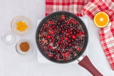 Cranberry sauce being heated up in a pan, close up view from above. Cranberry sauce recipe, cooking concept clipart