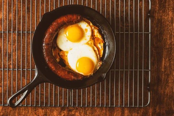 Fried eggs with sausage on frying pan close up on wooden background