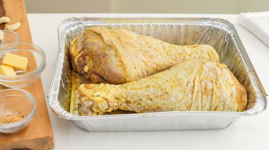 Terbiye edilmiş hindi bacakları tek kullanımlık bir tencere içinde beyaz mutfak masasına yakın, pişirilmeye hazır, kapatılmaya hazır.