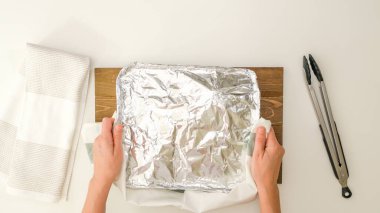 Şef alüminyum folyoyu çıkarıyor. Baharatlı terbiye edilmiş hindi bacakları tek kullanımlık bir tencerede pişirilmiş, fırından yeni çıkmış, yukarıdan yakın görüş. Adım adım kızartılmış hindi tarifi