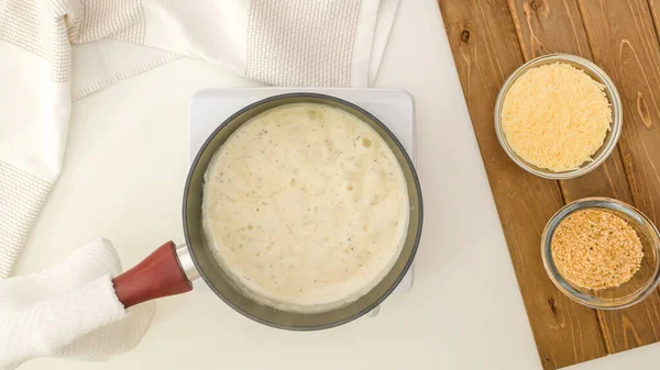 Tencereli Alfredo sosu, düz. Kremalı Alfredo soslu kuşkonmaz güveci üzerine ekmek kırıntıları ve adım adım parmesan peyniri..