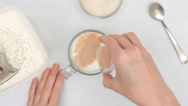 Dissolving dry yeast in warm milk. Step by step flat bread recipe, baking process. Close up view from above, woman hands