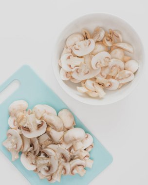 Taze kesilmiş organik beyaz mantarlar beyaz arka plandaki kesme tahtasına, düz yere, dikey panoya kapanıyor.