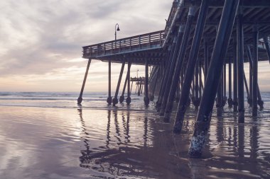 Sunset in pink color. Pacific ocean, wooden pier, and sun setting down the horizon. Pismo Beach, California