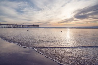 Sunset in pink color. Pacific ocean, wooden pier, and sun setting down the horizon with beautiful sun reflections on water. Pismo Beach, California