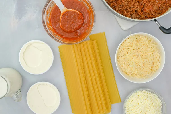 Pişmemiş lazanya makarna, çeşit çeşit peynir, marinara sosu ve kıyma, lazanya tarifi için malzemeler mutfak masasına yakın.