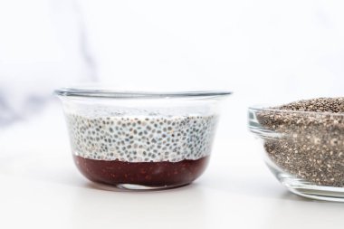 Cam bir kasede ahududu reçelli Chia tohumu pudingi. Beyaz arka plana yakın.