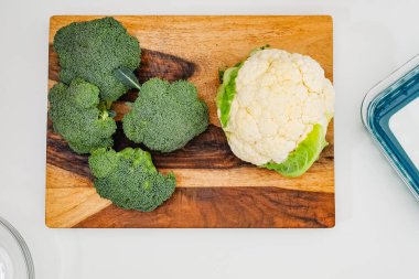 Karnabahar ve brokoli, açık gri arka planda yukarıdan ahşap kesme tahtasına yakın.