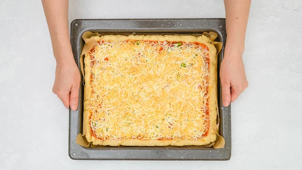 Uncooked vegetarian pizza on baking pan in woman's hands, close up view from above, copy space