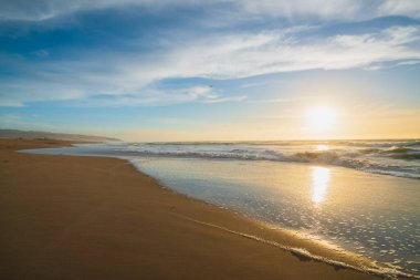 Sahilde gün batımı. Güzel sakin bir kumsal manzarası, turkuaz renkli su ve bulutlu gökyüzü.