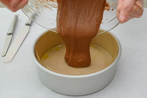 Cake pan lined with parchment paper close up on kitchen table, pouring cake batter into the pan. Chocolate cake step by step recipe, close up baking process