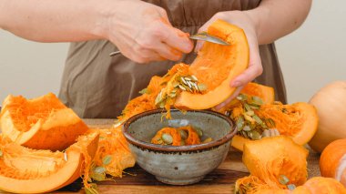 Kadın eli kaşık kullanarak balkabağının tohumlarını çıkarıyor. Adım adım yaklaş, kabak püresi yap.