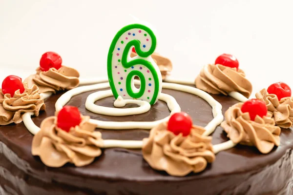 Birthday chocolate cake with candle in the form of number Six. Homemade cake decorated with chocolate cream and cherries close up on white background