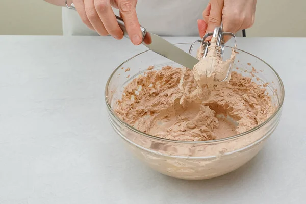 The chocolate cake frosting  for Chocolate Cake close up in a bowl. Beating cream using an electric hand mixer, close up on kitchen table, woman hands