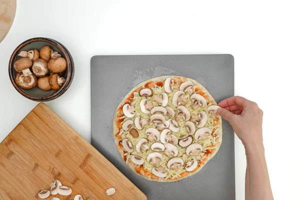 Topping pizza dough mushroom slices, close up view, flat lay, woman hands. Homemade mozzarella-mushroom pizza step by step recipe