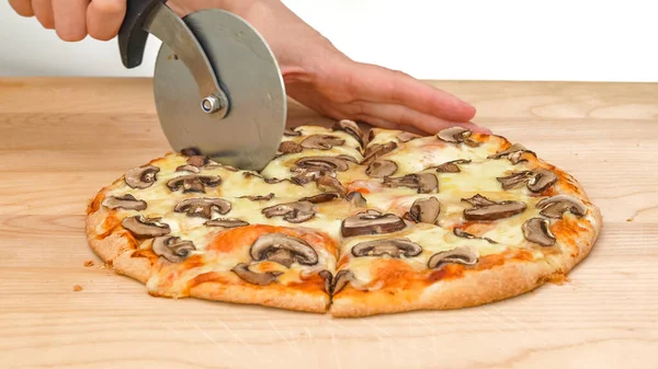 Woman cuts mushroom pizza using a pizza cutter, close up on wooden cutting board on white background