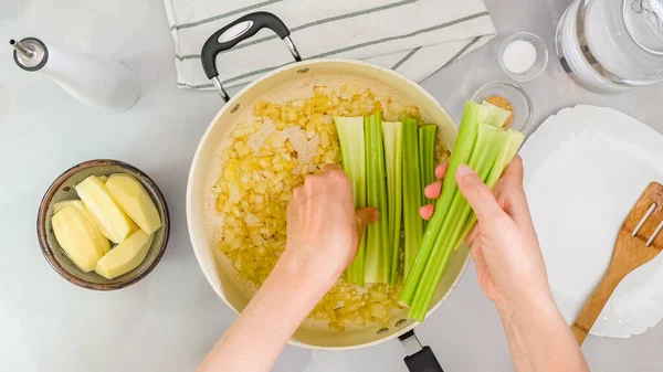Celery soup recipe. Woman hands placing fresh green celery in a pot, close up view from above