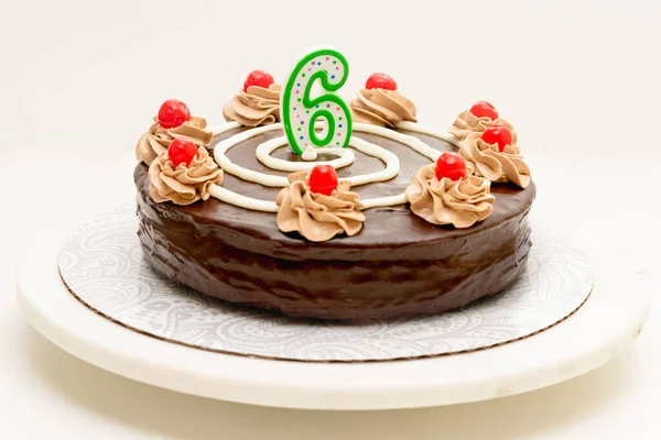Birthday chocolate cake with candle in the form of number Six. Homemade cake decorated with chocolate cream and cherries close up on white background
