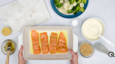 Fırın kabında marine edilmiş somon filetosu, karnabahar, brokoli ve Alfredo sosu mutfak masasında, düz bir şekilde. Yemek pişirme süreci, tarif, kadın elleri