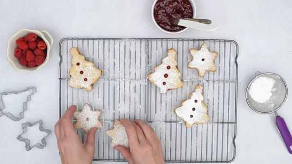 Christmas shortbread cookies with raspberry jam recipe, close up baking process. Baked cookies close up on cooling rack, woman hands, flat lay