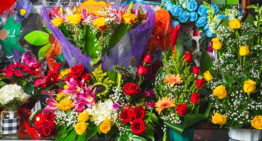 Vibrant collection of mixed flower arrangements including roses, lilies, sunflowers, and gerberas in a market display.