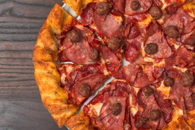 A loaded pizza featuring pepperoni, sausage, ham, and bacon over melted cheese and crispy crust.