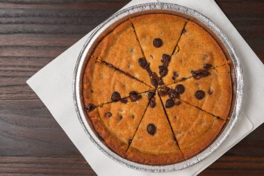 A warm, gooey chocolate chip cookie dessert baked in a round tin and cut into slices.