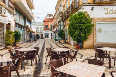 Olhao, Portekiz, 12 Ekim 2025. Boş kafe masaları, yerel dükkanlar ve eski mimarilerle çevrili geleneksel fayanslı yaya caddesinde oturuyor..