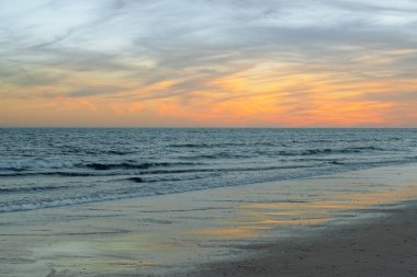 Sakin dalgalar sahile vurur pastel renkler alacakaranlıkta gökyüzünü doldurur.