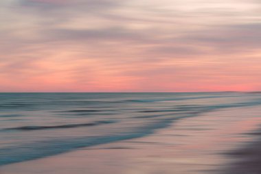 Uzun bir pozlama dalgaları ve gökyüzünü bulanıklaştırır ve huzurlu bir kıyı şeridi boyunca yumuşak pastel tonlara dönüştürür..