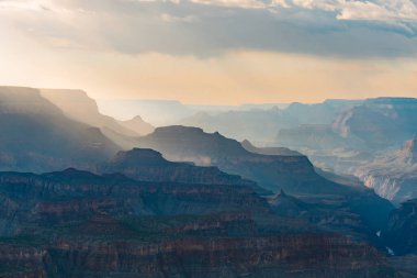 Yumuşak güneş ışığı bulutların arasından süzülür Büyük Kanyon 'un katmanlı sırtlarının üzerinden..