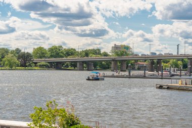Washington D.C. USA, 24 Mayıs 2025. Araçlar Potomac nehri üzerindeki köprüden geçerken küçük bir tekne rıhtıma yanaşıyor..