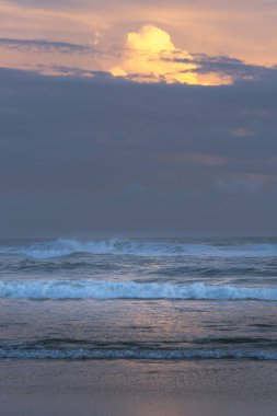 Okyanus dalgaları yükselen altın bir bulutun altında alacakaranlık denizin üzerinde batarken