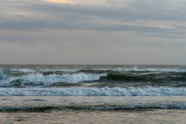 Kuvvetli dalgalar denizin üzerinde ağır, gri, mavi bir alacakaranlık gökyüzünün altında hareket eder.