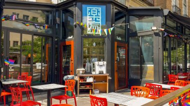 Washington D.C. USA - 24 Mayıs 2025. Parlak kırmızı verandalı bir kafe güneşli bir sokakta toplanmış bir grup insanın yanında duruyor..