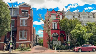 Washington D.C., ABD, 24 Mayıs 2025. Yapraklı bir sokak köşesindeki tarihi kırmızı ve beyaz evler arasında dar bir ara sokak var..